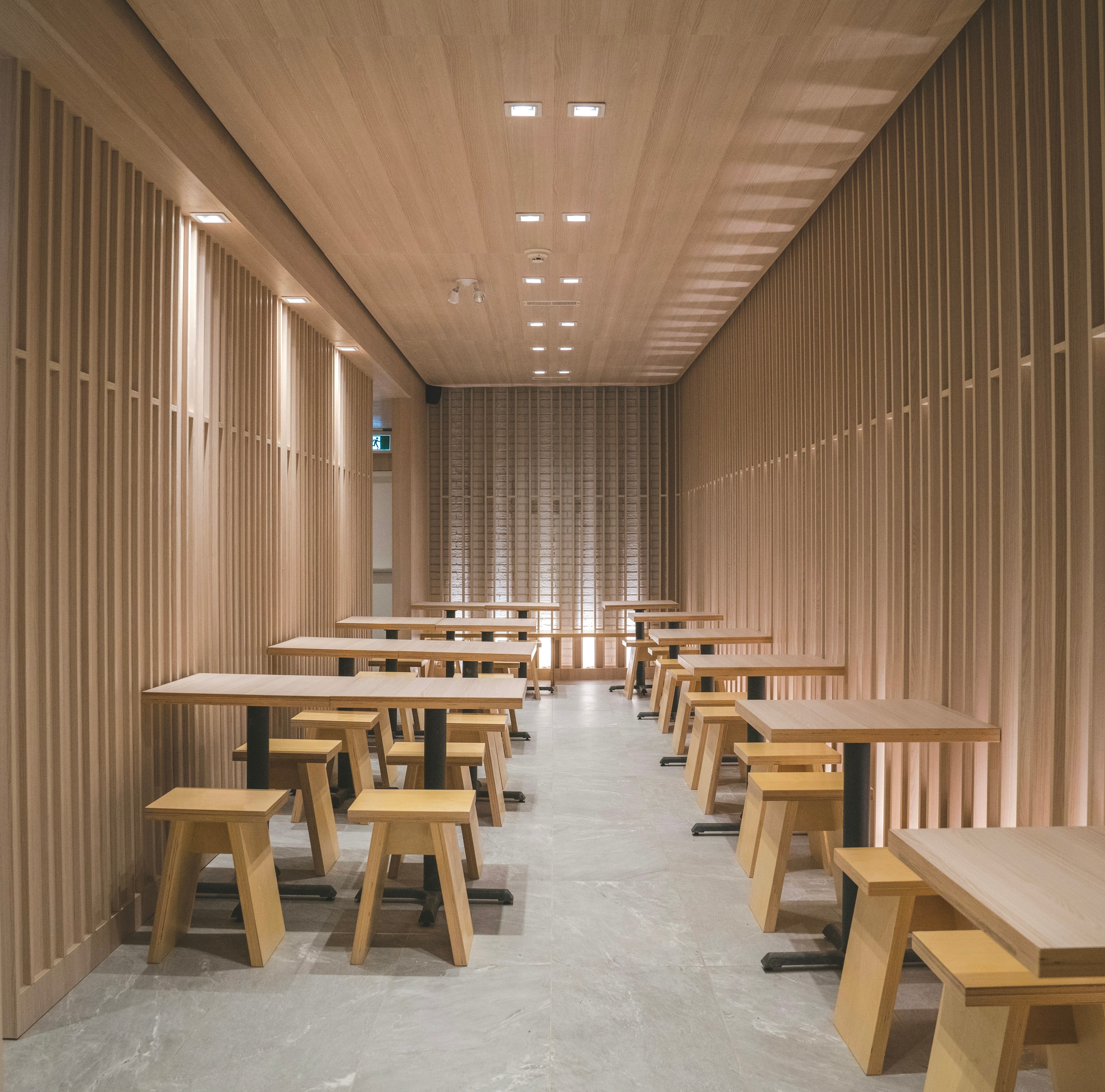 A long timber-lined room with rows of tables and stools beneath recessed lighting.
