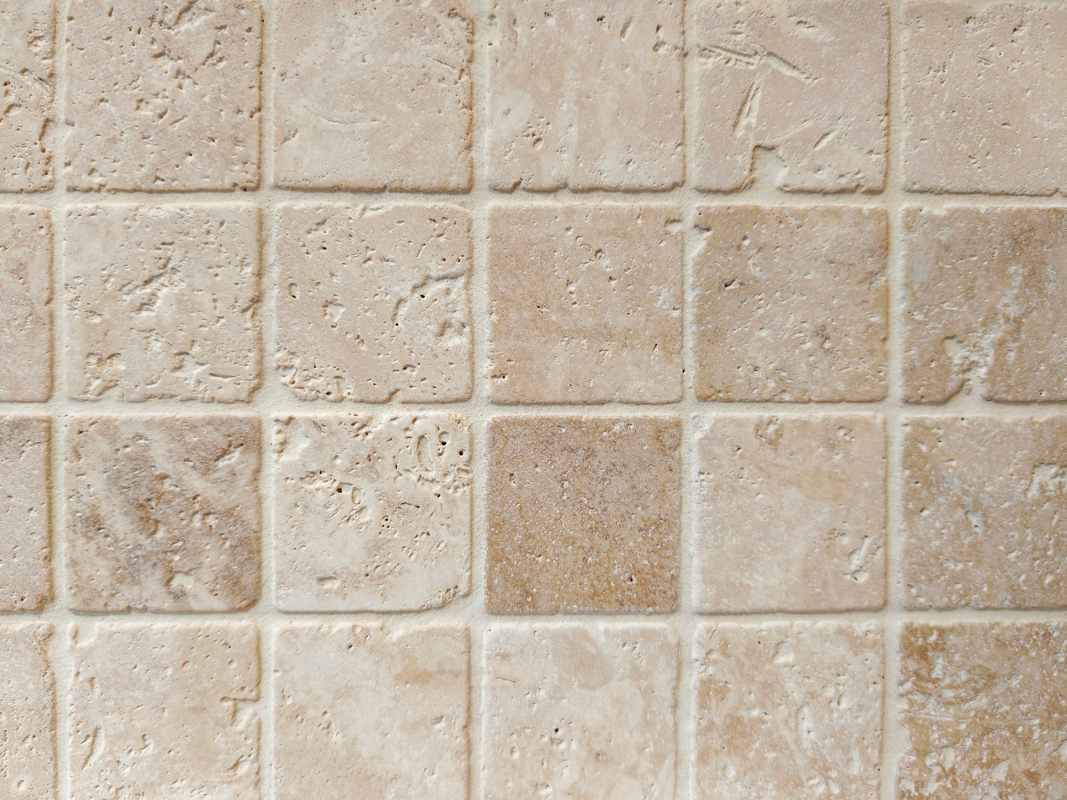 Travertine tiling laid in a regular grid, its natural pitting and veining raked by side light.