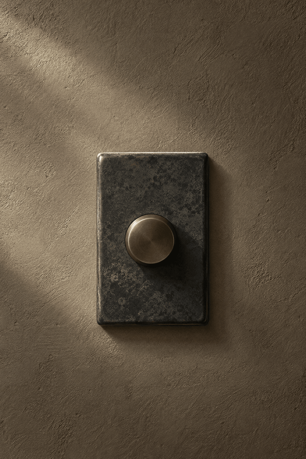 An iron-glazed ceramic rotary dimmer with a sculptural bronze dial on warm taupe plaster.
