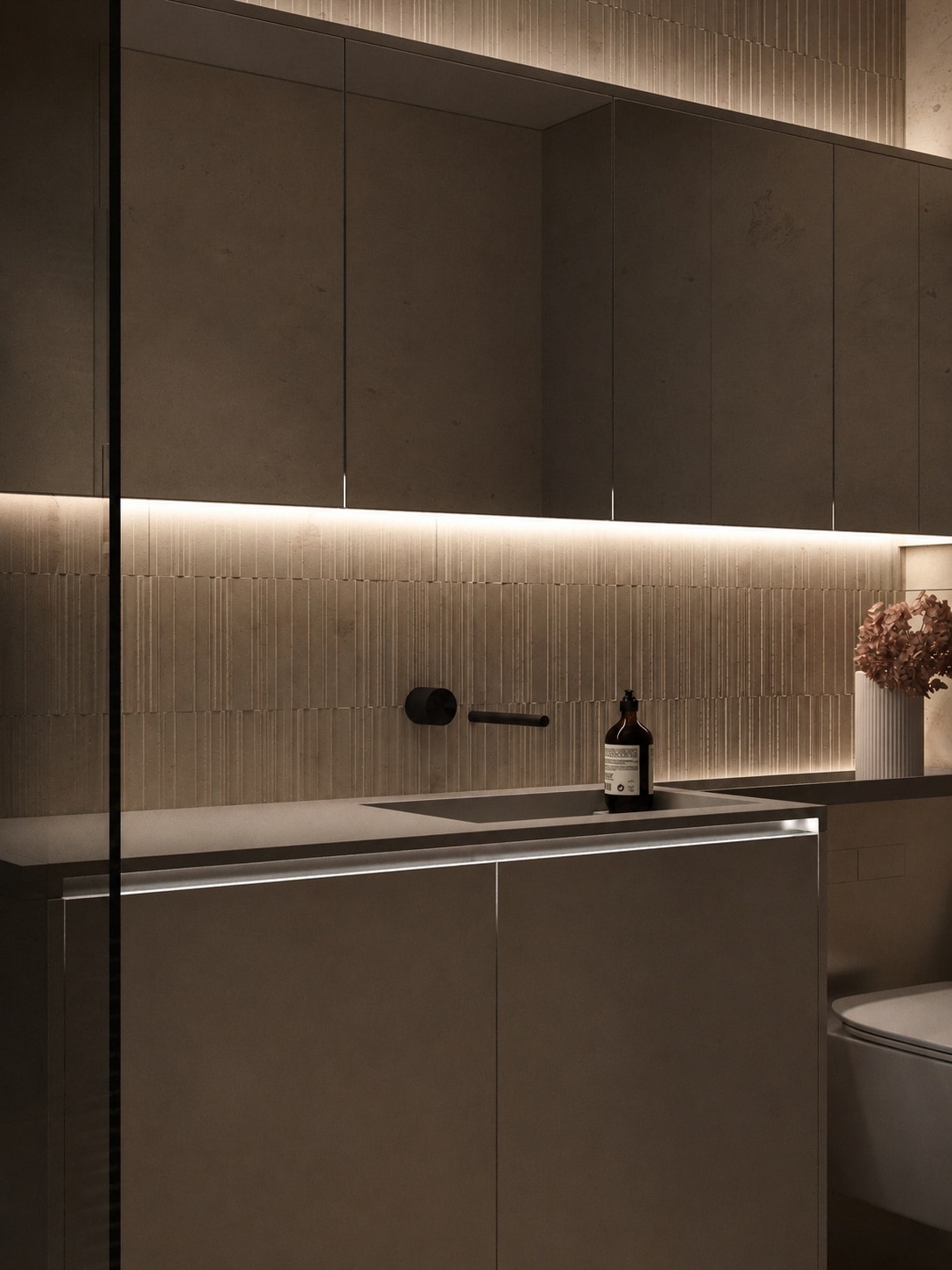 A dark stone vanity counter with black tapware, seen at an angle, with a wall-hung WC beyond.