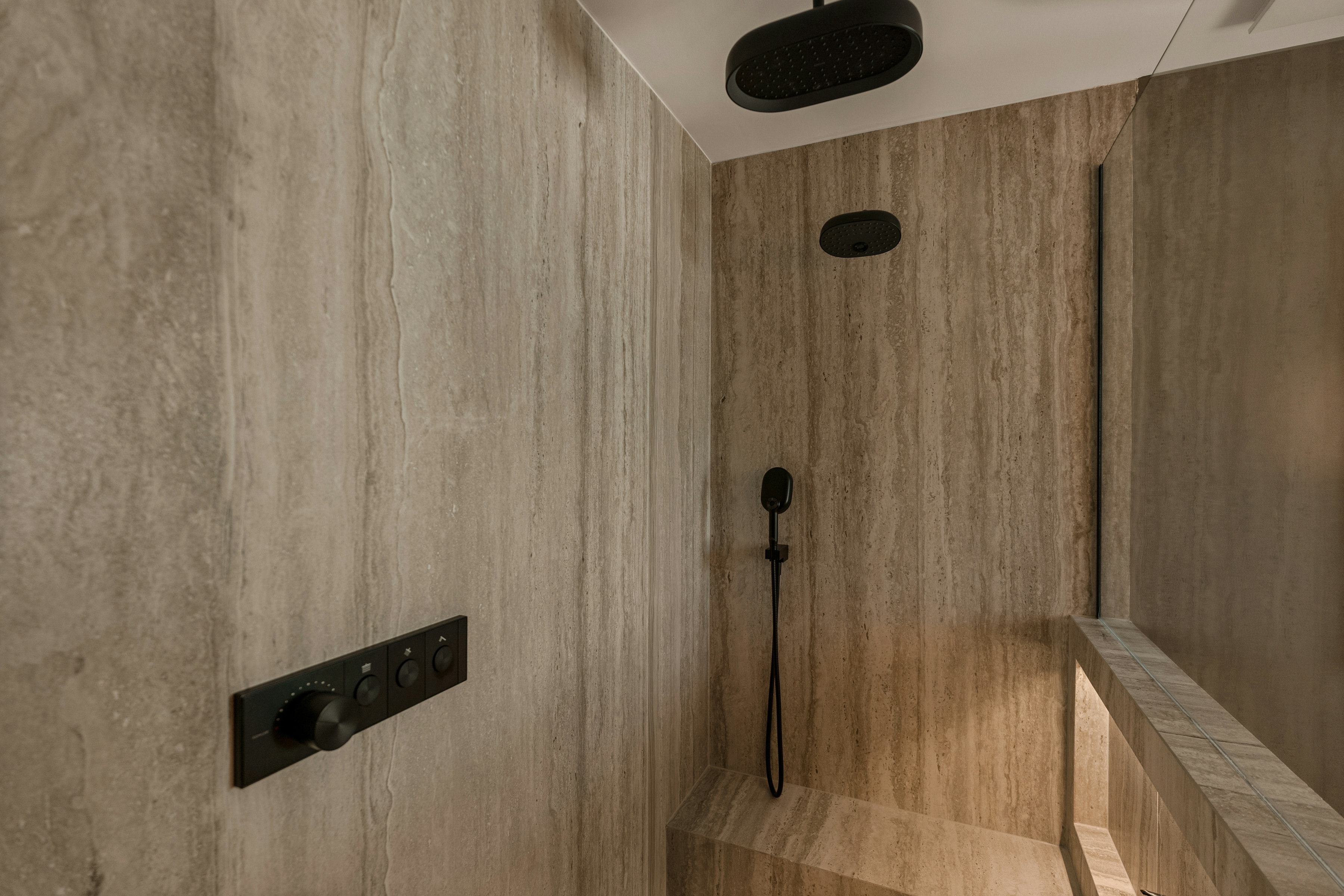 Detail of a stone-lined wet area, showing the junction between wall panel and shower screen.